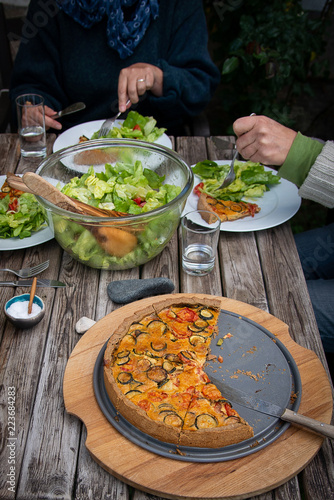 People eat healthy salad and quiche or pie on wooden table, outdoors. Dining together, in cozy, nice atmosphere