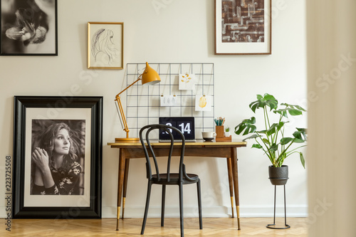 Large, framed photo and a monstera plant in a classic workspace interior with an orange lamp on a wooden desk