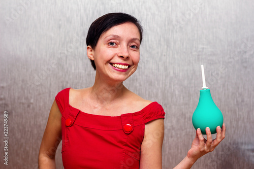 Smiling and happy woman holding an enema isolated by gray background.