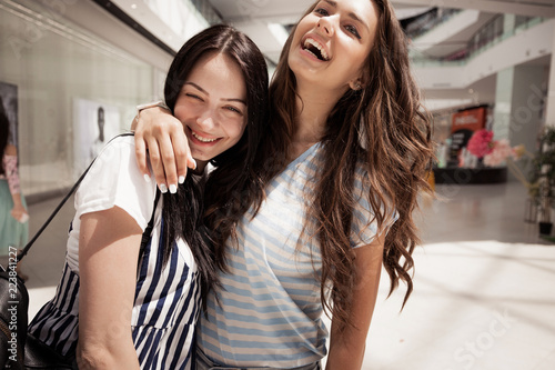 Two young pretty dark-haired girls,wearing casual outfit,hug each other in a lobby.