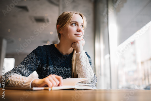 Young attractive university student studying at modern library. Cute caucasian woman with beautiful blue eyes sitting in loft cafe, planning working process, thinking about project. Exam preparation