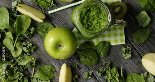 From above shot of green composition with fresh ripe apple and kiwi slices on wooden table with smoothie in jar and fresh greens