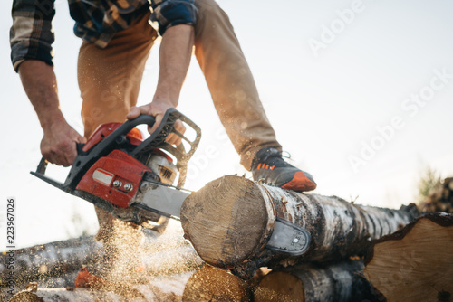 Professional lumberman sawing trees on sawmill. Close-up view on chainsaw in hands