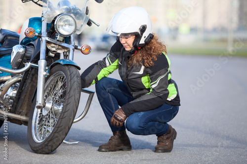 Woman biker trying to repair flat tire on motorcycle at city asphalt road