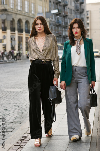 Outdoor full body portrait of two young beautiful fashionable women wearing stylish trendy clothes, shoes and accessories walking in street of european city. Street fashion concept