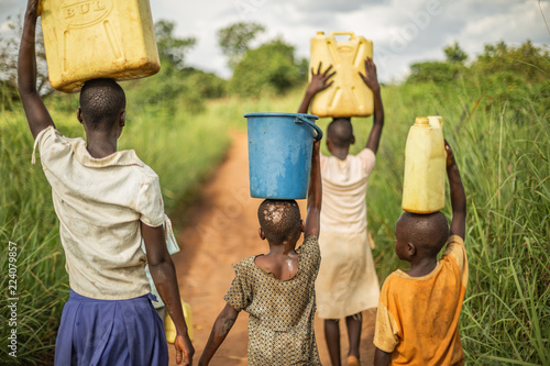 Group of young African kids walking with buckets and jerrycans on their head as they prepare to bring clean water back to their village.