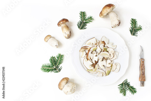 Autumn styled food arrangement. Composition of whole and sliced porcino mushrooms, Boletus edulis on white plate, fir branches and pocket knife. White table background. Fall design, flat lay, top view