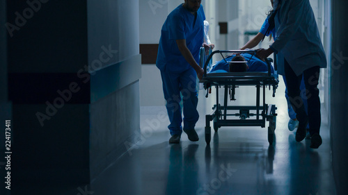 Emergency Department: Doctors, Nurses and Paramedics Push Gurney / Stretcher with Seriously Injured Patient towards the Operating Room.