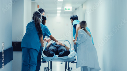 Emergency Department: Doctors, Nurses and Paramedics Push Gurney / Stretcher with Seriously Injured Patient towards the Operating Room. Bright Modern Hospital with Professional Staff Saving Lives.