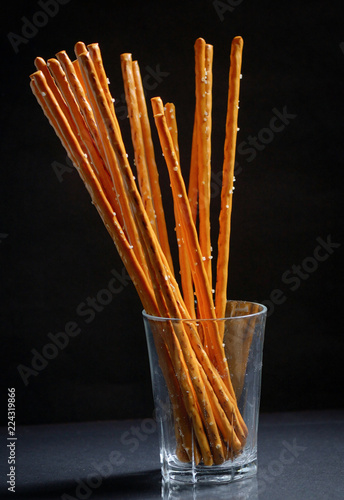 Pretzel sticks in small glass on black background