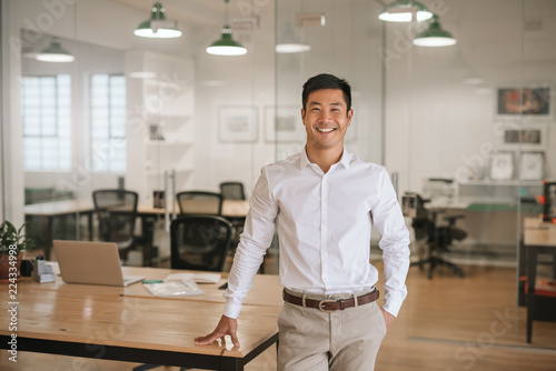 Young Asian businessman standing in an office smiling confidently