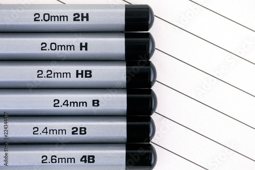 Gray graphite pencils with graphite grading scale in a row on lined paper.