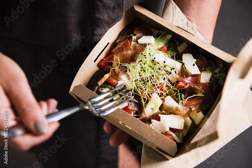 Woman's hand is holding a take away fresh salad in a lunch box. Gourmet conception.