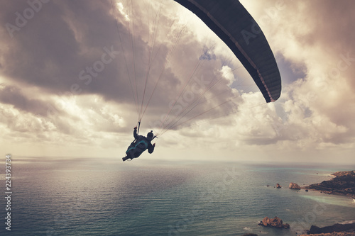 Silhouette of a man flying on a paraglider high above the sea in the clouds, sport, beauty and freedom concept