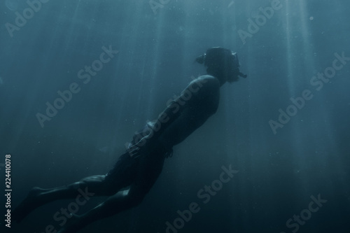 Man swimming underwater among sunbeams.