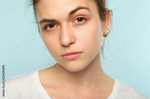 emotion face. suspicious thoughtful dubious distrustful woman raising a brow. young beautiful brown haired girl portrait on blue background.