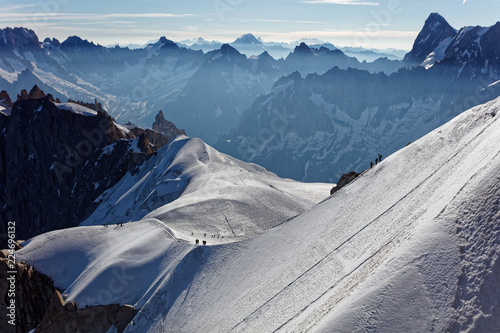 Chamonix, south-east France, Auvergne-Rhône-Alpes. Climbers heading for Mont Blanc. Descending from Aiguille du Midi cable car station towards sunny snow planes and glaciers on border of France