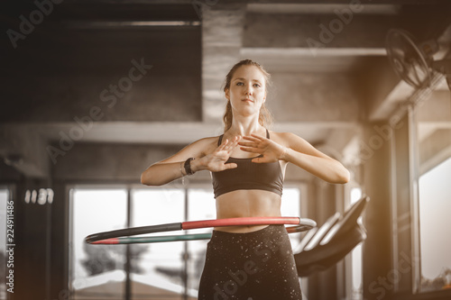 Beautiful caucasian young woman doing hula hoop in step waist hooping forward stance. Young woman doing hula hoop during an exercise class in a gym. Healthy sports lifestyle, Fitness, Healthy concept.