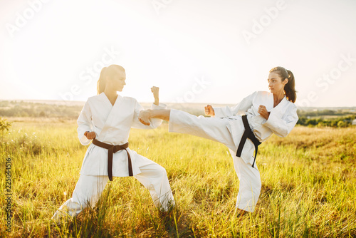 Two female karate in kimono fight in summer field