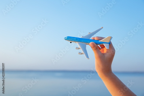 A hand holding a toy aircraft above the water at sunset
