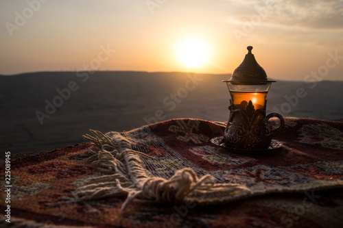 Arabska herbata w szkle na wschodnim dywanie. Koncepcja wschodniej herbaty. Puchar tradycyjny Armudu. Zachód słońca w tle. Selektywne ustawianie ostrości