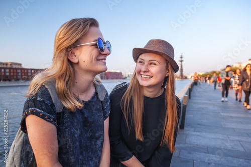 Two young happy girlfriends student teenagers rest together on the waterfront by the river