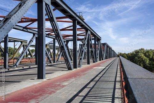 Germany, Hanau, Steinheim: Street scene view of empty car free metal bridge with red bikeway with blue sky - concept traffic transport construction architecture nature environemt climate change