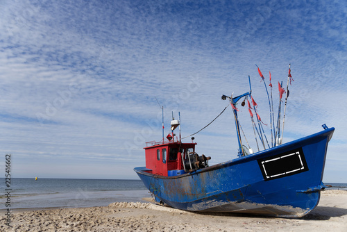 A blue fishing boat standing on the sandy shore of the sea.