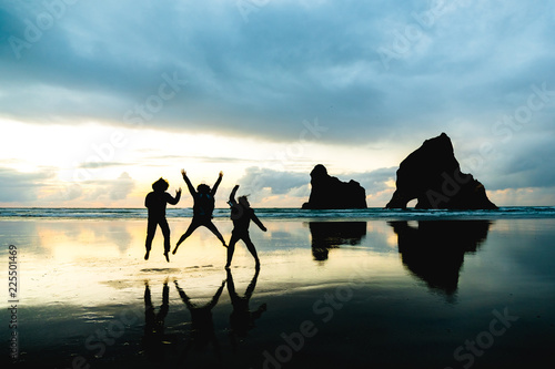 A group of people taking a photo with with famous rocks. Sunset scene golden light and silhouette. Wharariki Beach Nelson, South Island, New Zealand.