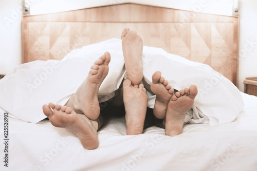 three pairs of feet lying together under bed cover in bedroom, threesome group sex concept, filtered image