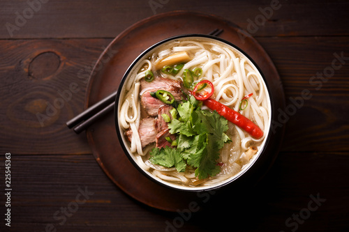 Vietnamese traditional soup Pho Bo with beef and fresh coriander on dark wooden background