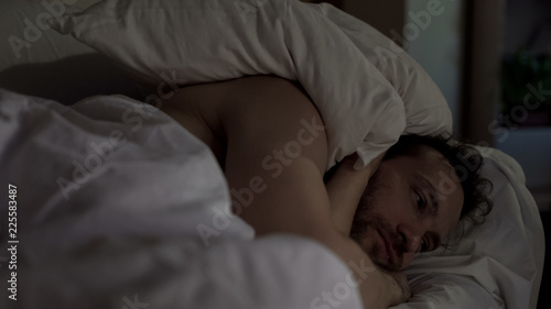 Annoyed man tossing and turning in bed unable to fall asleep, noisy neighbors