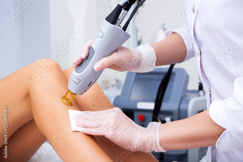 Close-up of a female cosmetologist in a medical coat making a young woman a procedure laser hair removal for leg. Cosmetology, ionization, diamond procedures.