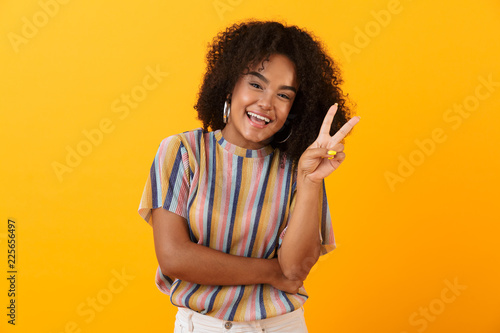 African cute girl posing isolated over yellow background make peace gesture.