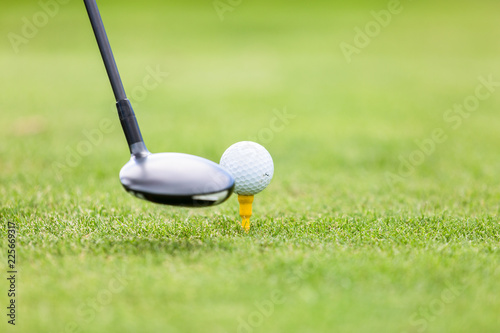 Close-up of golf ball on tee in front of driver on green field