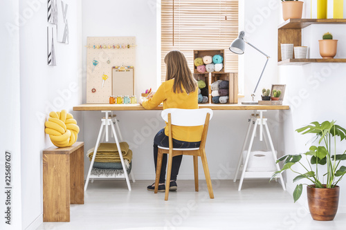 Woman sitting at a desk in a home office interior with knitting wool, organizer and yellow pillow