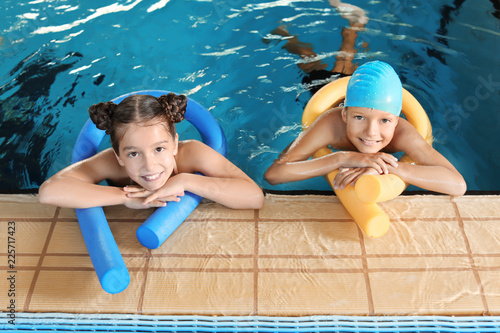 Małe dzieci z makaronem pływackim w krytym basenie