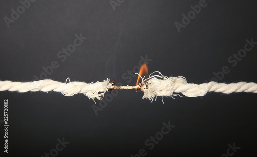 Burning frayed rope at breaking point on gray background