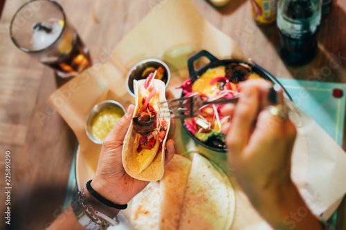 Young woman preparing and eating mexican food in a street restaurant. Mexican tacos, nachos and wings. Top view.