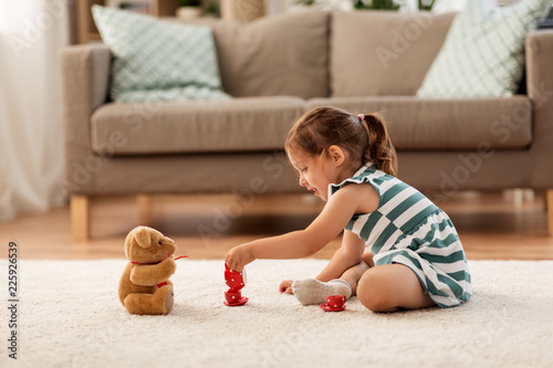 childhood and people concept - happy three years old baby girl playing tea party with toy crockery and teddy bear at home