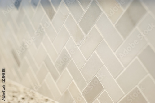 Close detail of a new small tile herringbone pattern professionally installed in a home kitchen. Warm grey tones. Horizontal image with shallow depth of field.