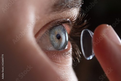 Close-up of a man putting contact lenses on blue eye. Concept of: healtcare, optic, hydration of the eye.