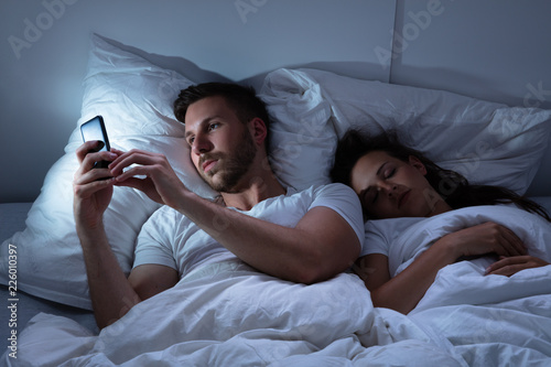 Man Using Cellphone While Her Wife Sitting On Bed