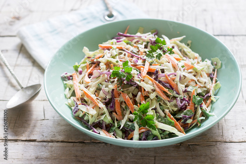 Coleslaw of cabbage, carrots and various herbs with mayonnaise in a large plate on a wooden background.