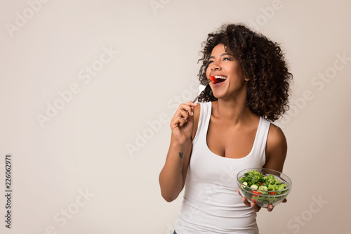 Excited lady eating healthy salad over light background