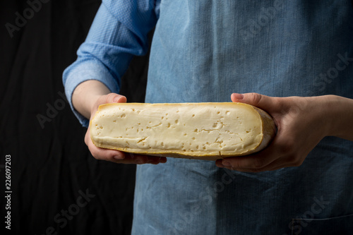 Woman in blue apron holding taleggio cheese on dark background