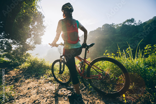 Young woman cyclist carrying mountain bike on summer forest trail