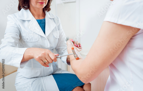 Neurological examination. The neurologist testing reflexes on a female patient using a hammer.