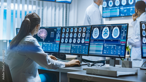 Team of Professional Scientists Work in the Brain Research Laboratory. Neurologists / Neuroscientists Surrounded by Monitors Showing CT, MRI Scans Having Discussions and Working on Personal Computers.