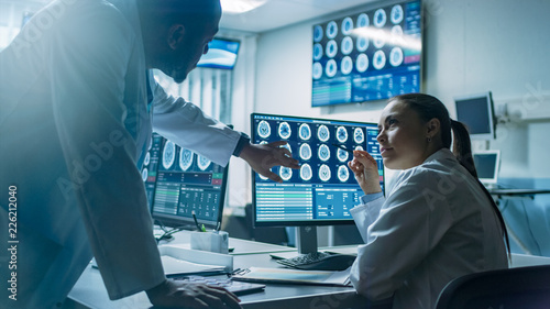 Two Scientists in the Brain Research Laboratory work on a Project, Using Personal Computer with MRI Scans Show Brain Anomalies. Neuroscientists at Work.